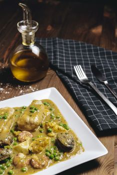 vertical photo of a healthy traditional spanish hake dish in green seafood sauce with clams, prawns, green peas and egg, typical mediterranean cuisine with rustic dark food style