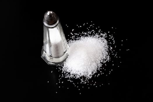 White Salt Shaker with Salt Pile On Black Background