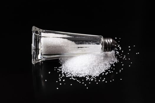 Salt shaker with pured salt crystals on black background