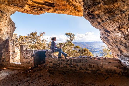 Female sitting in a cave cliff side with views over the valley seeking shelter from strong gale winds