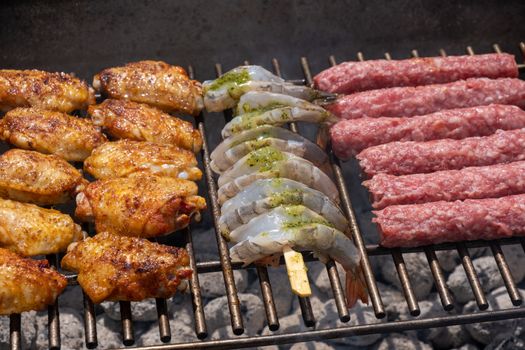 Mixed assortment of marinated meat, chicken, and prawns grilling on hot coals on a BBQ, summer outdoor party, delicious meal preparation