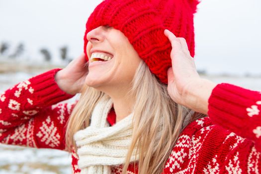 Happy woman in snow pulling beanie over eyes in a playful manner
