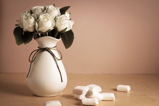 Copyspace with colorful mini marshmallows on a table next to white roses on a pink background