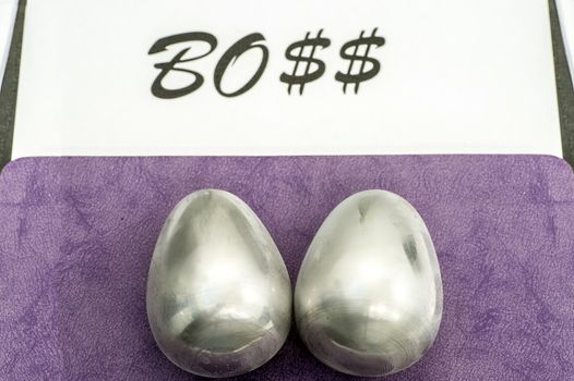 Two metal eggs on the office desk opposite the word Boss. The concept of power