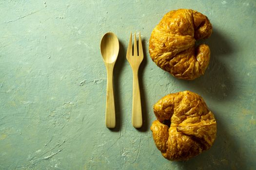 Top view croissants on wooden dish with spoon and fork on table. Copy space for text.