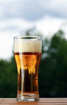 Nice high glass of beer with foam against nature background
