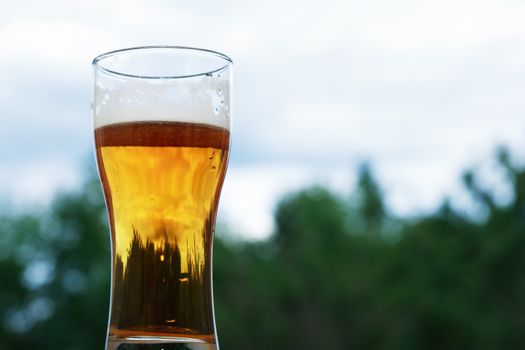 Nice high glass of beer with foam against nature background