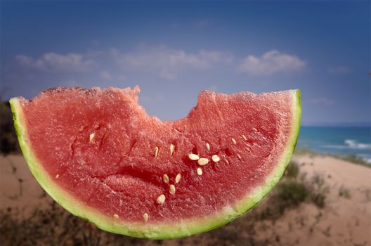 Slice of watermelon with bite and unfocused beach background