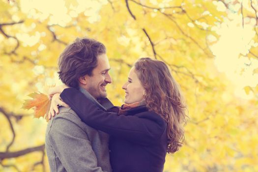 Smiling mid adult couple hug in autumn forest of yellow maple trees