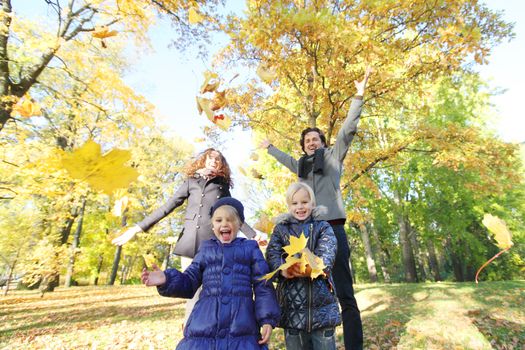 Happy family playing with autumn maple leaves in park at sunny day