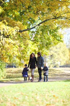 Happy family with two children walking in sunny autumn park holding hands