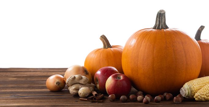 Autumn harvest still life with pumpkins , apples , hazelnut , corn , ginger , onion and cinnamon on wooden table isolated on white background