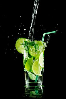 Pouring fresh mojito cocktail in glass isolated on black background