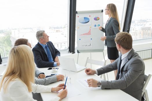 Businesswoman giving a presentation to her colleagues at work standing in front of a flipchart with diagrams