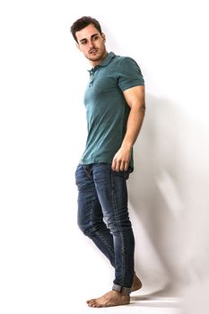 Handsome young man in green shirt and jeans posing isolated on white background in studio, full length shot
