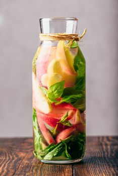 Bottle of Water Flavored with Sliced Peach and Basil Leaves. Vertical Orientation.