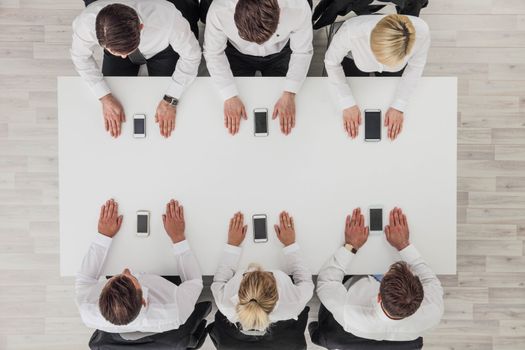 Top view of business people sitting around the table and using smartphones with blank screen