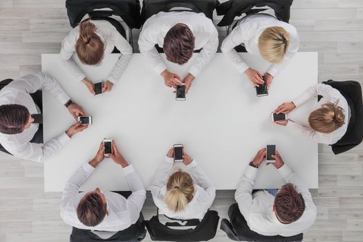 Top view of business people sitting around the table and using smartphones with blank screen