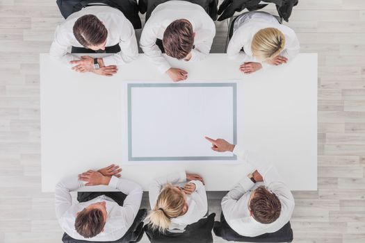 Business, people and team work concept - close up of creative team sitting at table and pointing finger to blank copy space for text