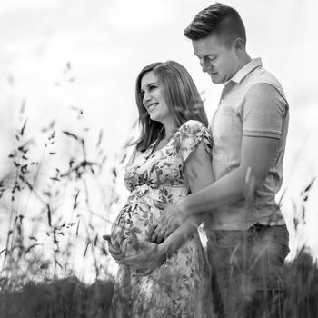 Young happy pregnant couple hugging in nature. Concept of love, relationship, care, marriage, family creation, pregnancy and parenting. Artistic black and white image.