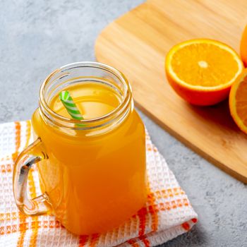 Freshly made citrus juice from oranges in a jar-mug with a straw close up on gray table .