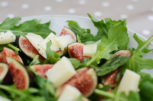 Fresh fig salad with pieces of salty pecorino and green rocket leaves in selective focus