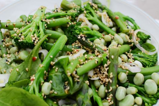 Tasty spring salad of baby broccoli, asparagus, broad beans, spinach leaves and shallot dressed with sesame and nigella seeds