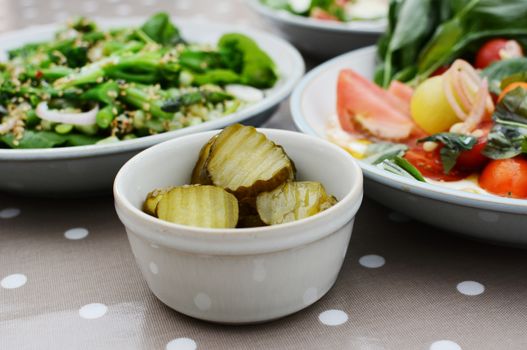 Tangy gherkin slices and fresh summer salads in selective focus on a dining table