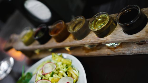 Set of shots in one row, six servings on a wooden stand and grren salad. Drink for the menu restaurant, bar, cafe