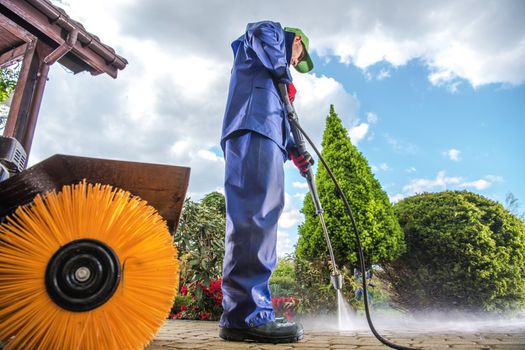 Men Wearing Industrial Wet Coat Cleaning Residential Driveway using Power Pressure Washer.