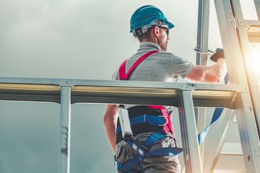 Caucasian Construction Contractor in His 30s Wearing Safety Harness. Steel House Building. Industrial Theme.