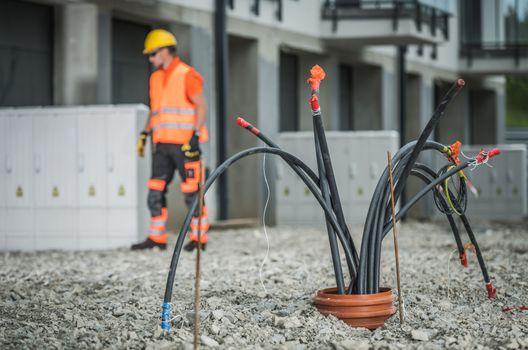 High Voltage Cables Installation. Bunch of Cables Comping From Underground Pipeline. Electric Technician in the Background.