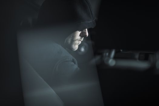 Caucasian Robber in Black Hood Waiting For a Good Moment Seating in a Car. Crime Concept Photo.