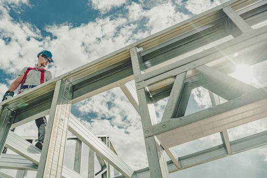 Skeleton Steel Construction. Caucasian Contractor with Power Tool in a Hand Working on Height Attached to the Frame by Safety Harness.