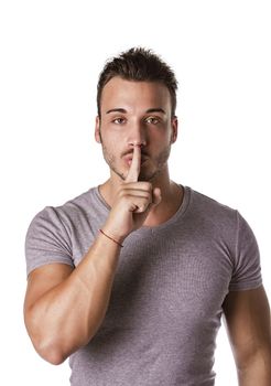 Attractive young man gesturing Hush or Silence with finger on mouth and nose, shushing isolated on white background