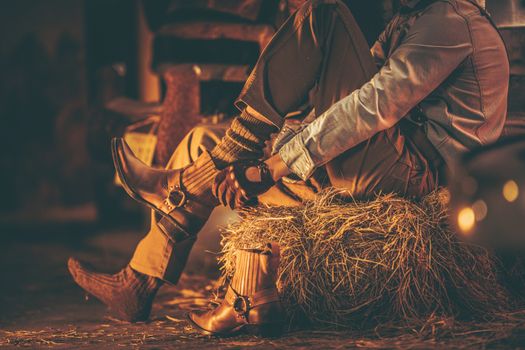 Cowboy in the Barn Wearing Boots While Seating on the Pile of Hay. American Farming Theme.