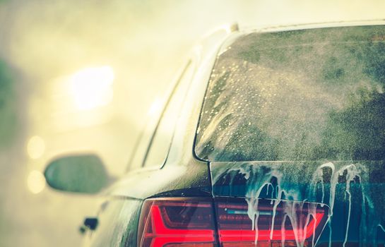 Cleaning Vehicle in the Car Wash. Closeup Photo. Auto Body Covered by Washing Detergent.