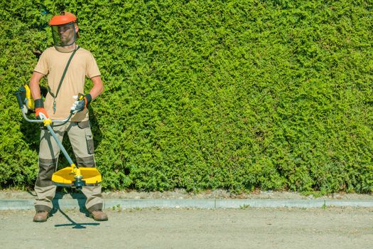 Gas String Trimmers Work. Caucasian Garden Worker with Power Tool.