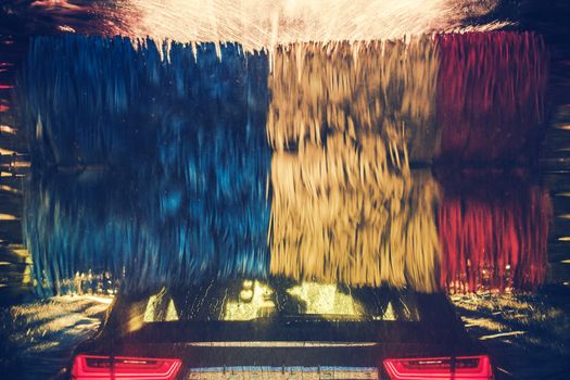 Colorful Car Wash in Action. Modern Vehicle Inside the Spinning Washing Brushes.