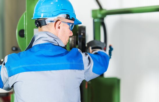 Professional Heavy Duty Machinery Operator. Caucasian Metalworking Industry Worker in Blue Hard Hat in Front of Machine Console. Industrial Theme.