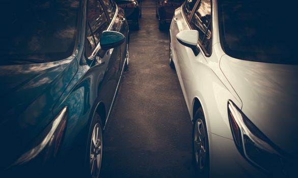 Tight Car Parking Spaces Theme. Modern Vehicles Side by Side Closeup Photo.