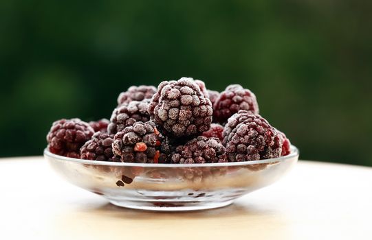 Saucer with heap of frozen blackberry fruits on wood