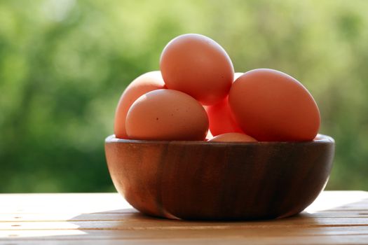 Heap of chicken eggs in wooden bowl against green nature background