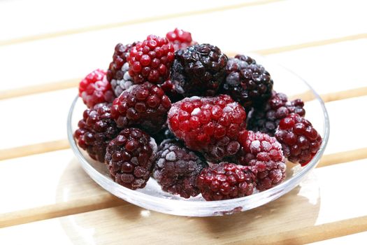 Saucer with heap of frozen blackberry fruits on wood