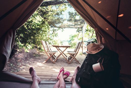 view of the legs of a hiker man with a kid resting barefoot in a camping tent, travel discovery concept, point of view shot