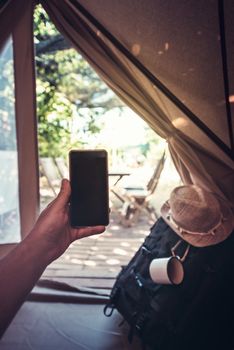 vertical view of a hand of a hiker person resting while consulting the phone in a camping tent, travel discovery concept, point of view shot