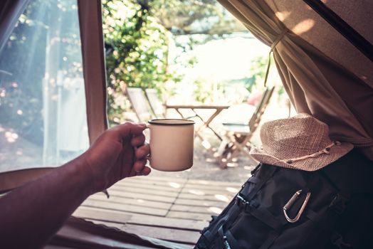 view of a hand of a hiker man resting with a cup in a camping tent, travel discovery concept, point of view shot