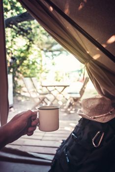 vertical view of a hand of a hiker man resting with a cup in a camping tent, travel discovery concept, point of view shot