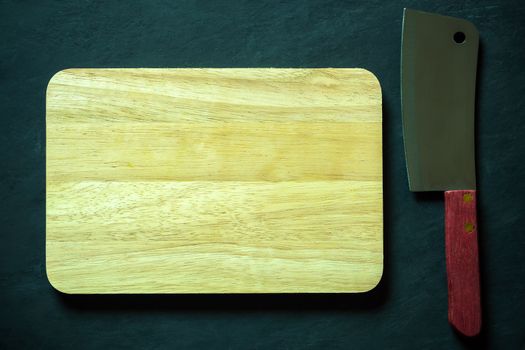 Wooden cutting board and Chinese chef knife on black cement floor. Top view and copy space for text. Concept of kitchenware and cooking.