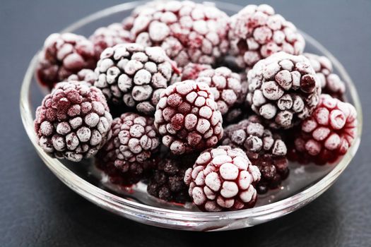 Saucer with heap of frozen black berry fruits on dark background